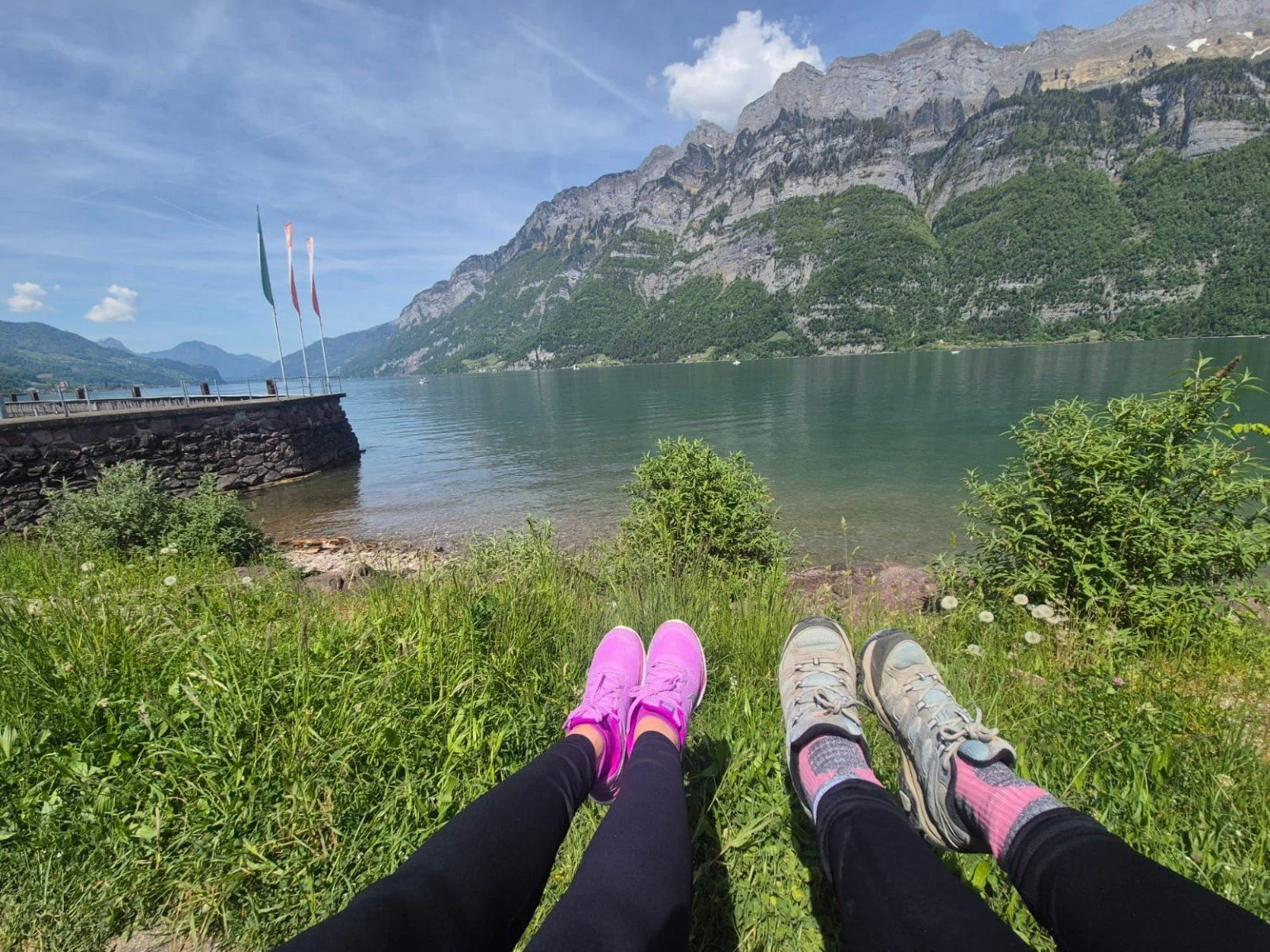 Feet stretched out on the grass beside a lake, with mountains beyond.