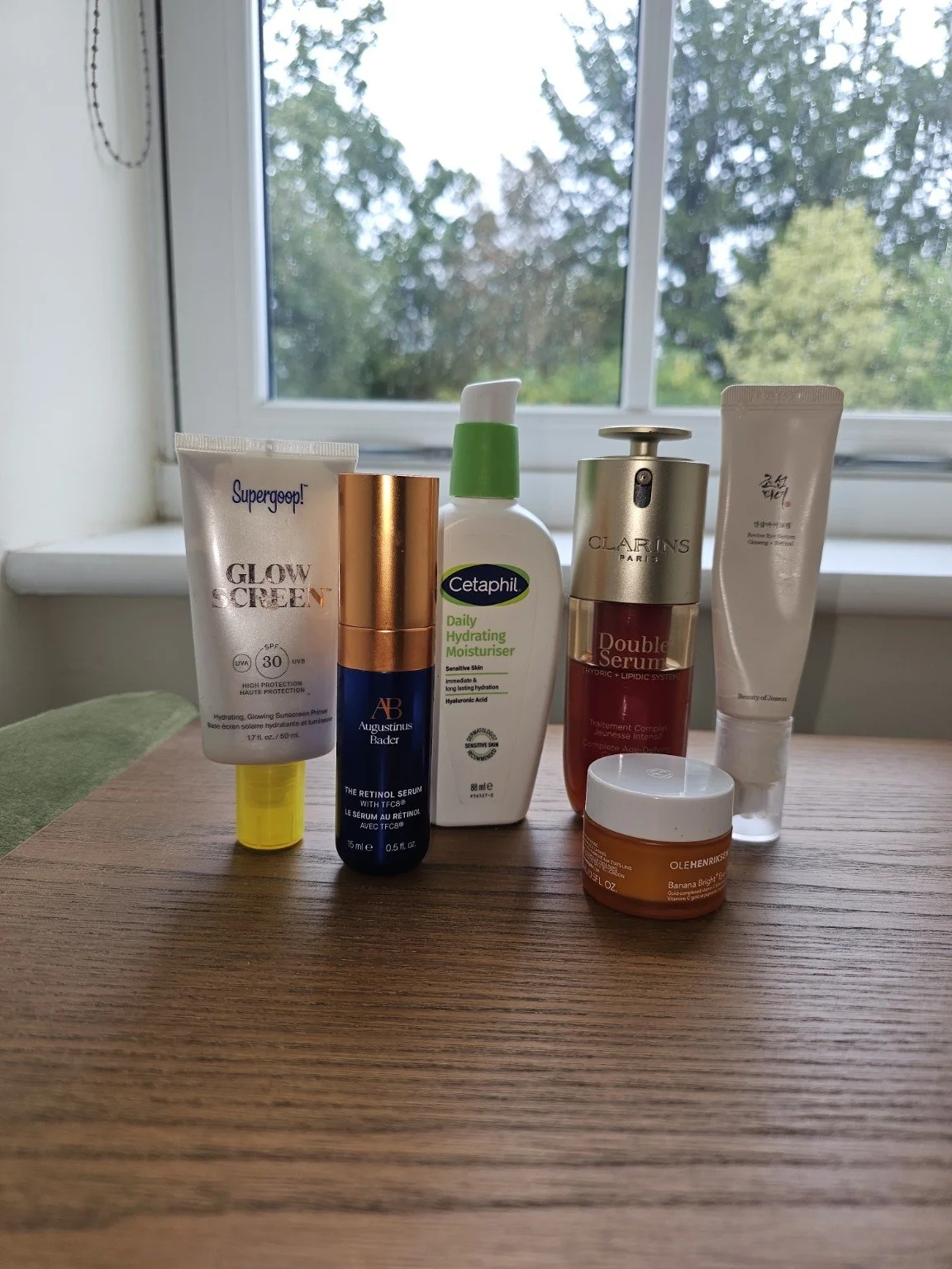 My skincare products arranged on a wooden surface beside the window.