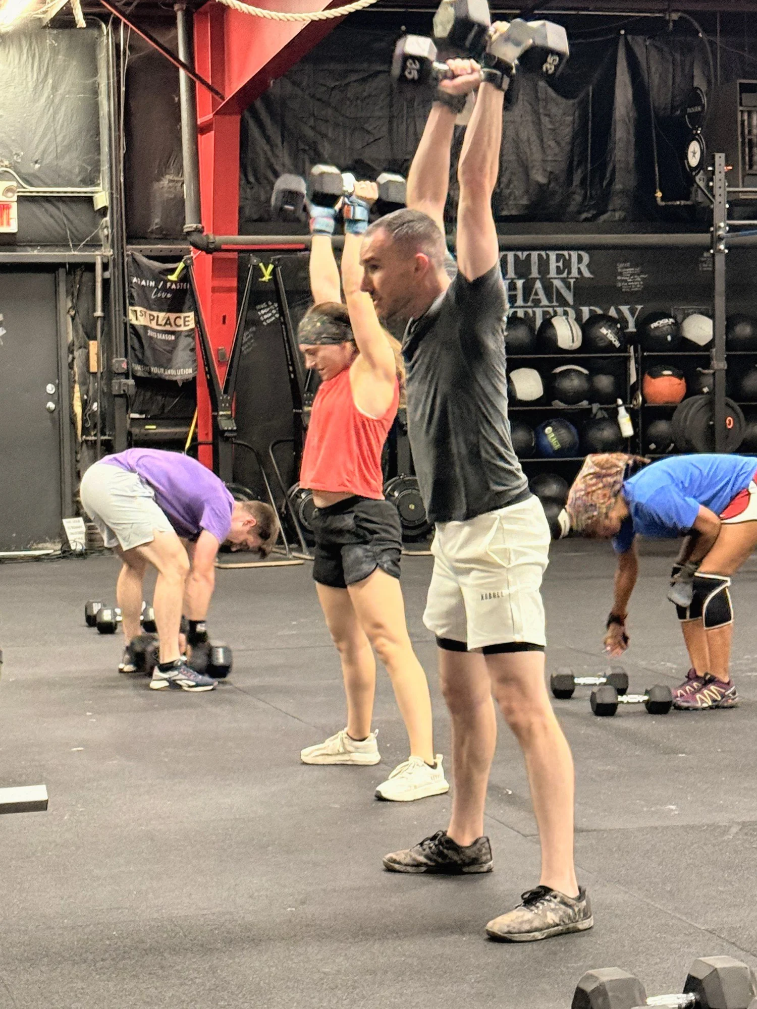 Adults lifting dumbbells overhead during a DFX CrossFit class