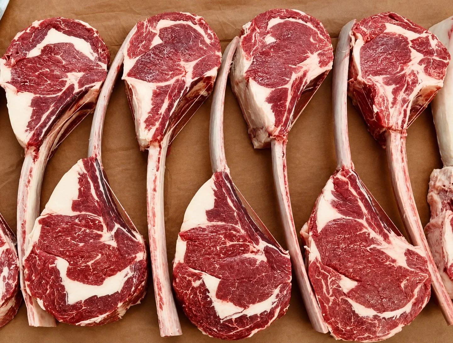 Raw tomahawk steaks with marbled beef and long rib bones, arranged on butcher’s paper