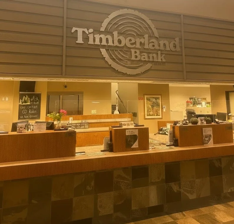 Timberland Bank interior reception wall ID — dimensional brand identity behind the teller line at a Western Washington branch, fabricated by Plumb Signs with brand-matched paint and finish program