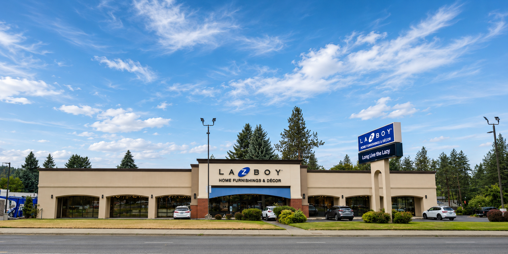 Wide view of the La-Z-Boy Spokane storefront on N Division Street showing the new face-lit channel-letter wall sign and the re-faced double-face pylon in context, fabricated and installed by Plumb Signs
