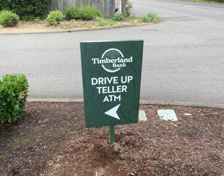 Timberland Bank exterior directional sign — non-illuminated aluminum panel with brand-matched satin finish guiding customers to the drive-up lane and parking entrance at a Western Washington branch