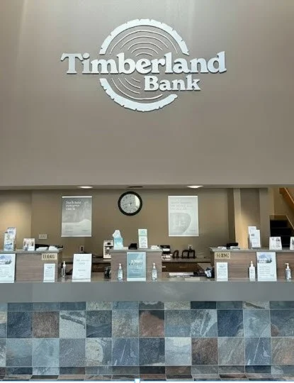 Timberland Bank Auburn, WA branch interior — refreshed reception and lobby brand identity with dimensional wordmark, ADA wayfinding, and brand-matched finishes installed by Plumb Signs