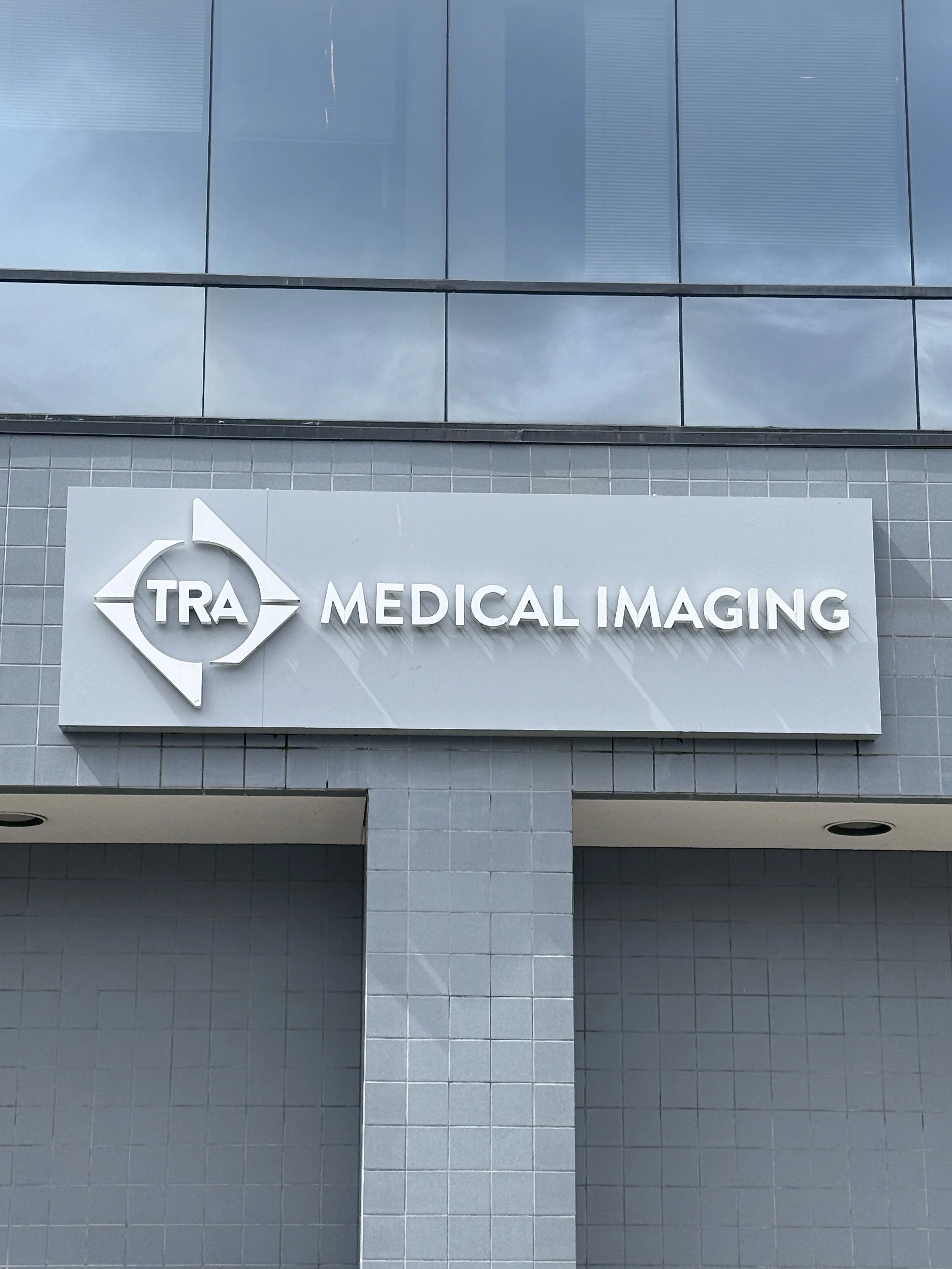 Exterior building cabinet sign reading TRA MEDICAL IMAGING in dimensional letters on the gray tile and curtainwall facade of the 4700 Point Fosdick Dr NW building in Gig Harbor, Washington — fabricated and installed by Plumb Signs
