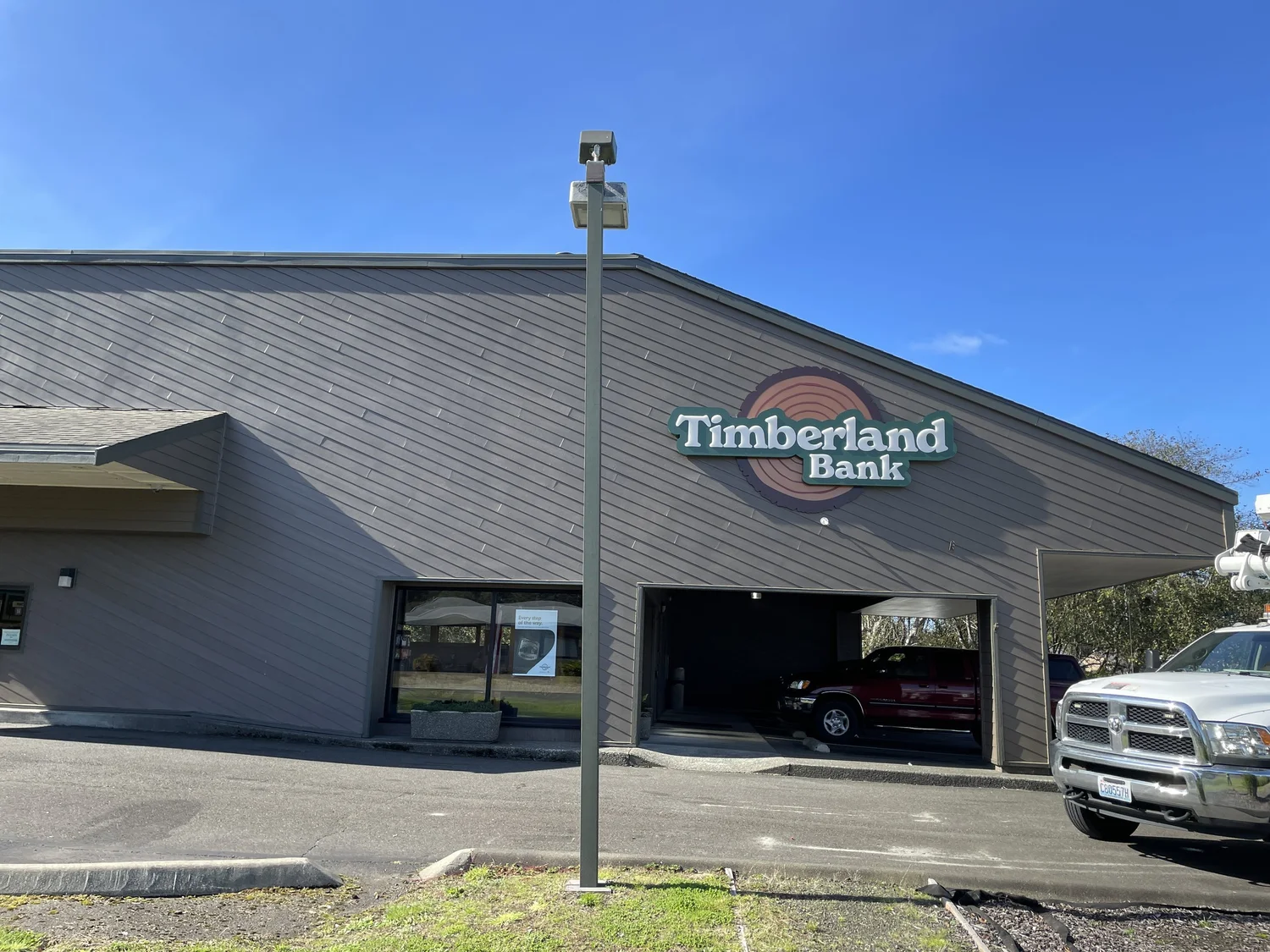 Timberland Bank exterior wall identification — dimensional flat-cut aluminum wordmark with tree icon, stud-mounted off the branch building face in the refreshed Timberland Bank brand standard