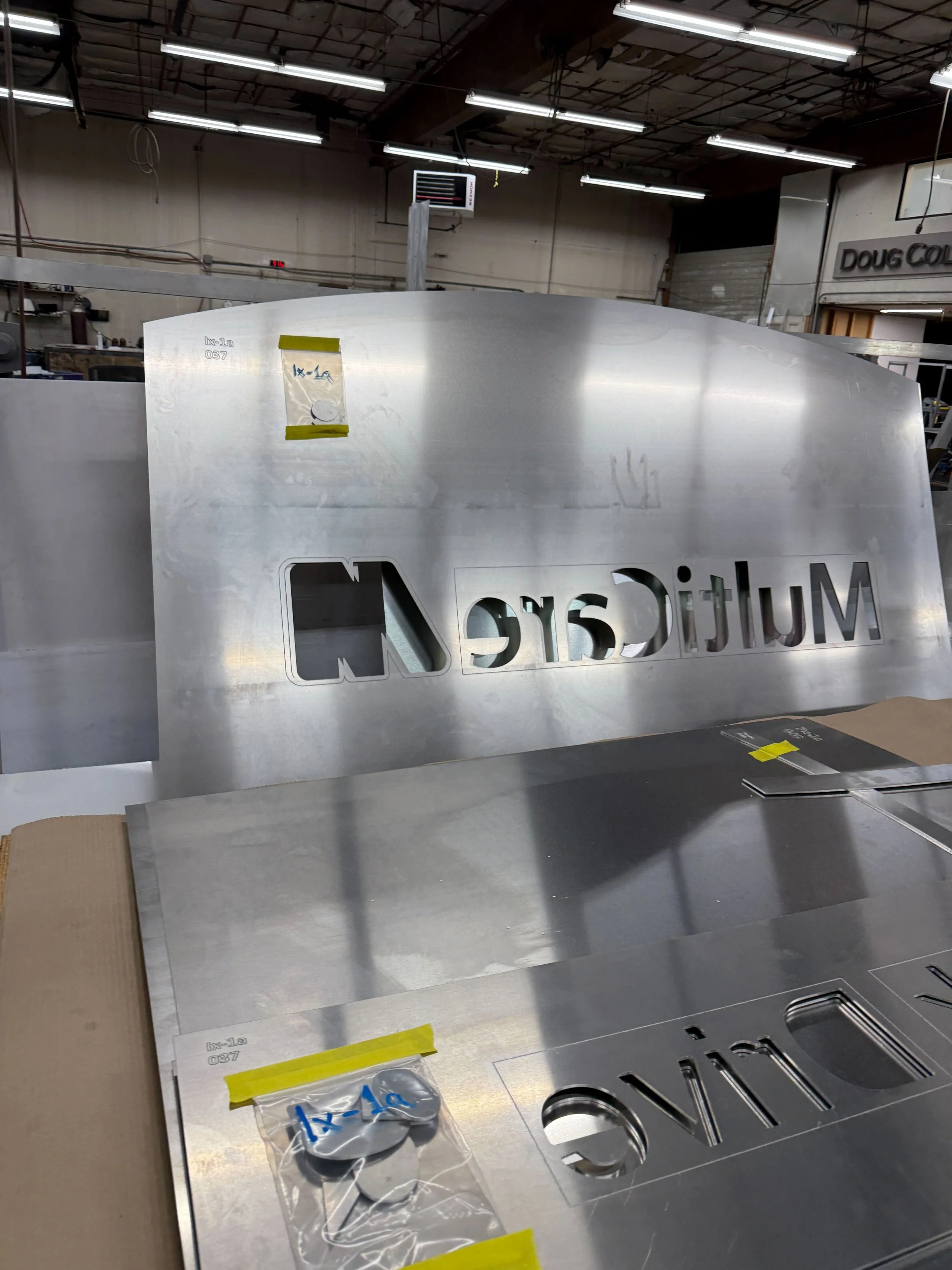 Laser-cut aluminum monument face with the MultiCare wordmark cutout on the fabrication bench at the Plumb Signs Tacoma shop