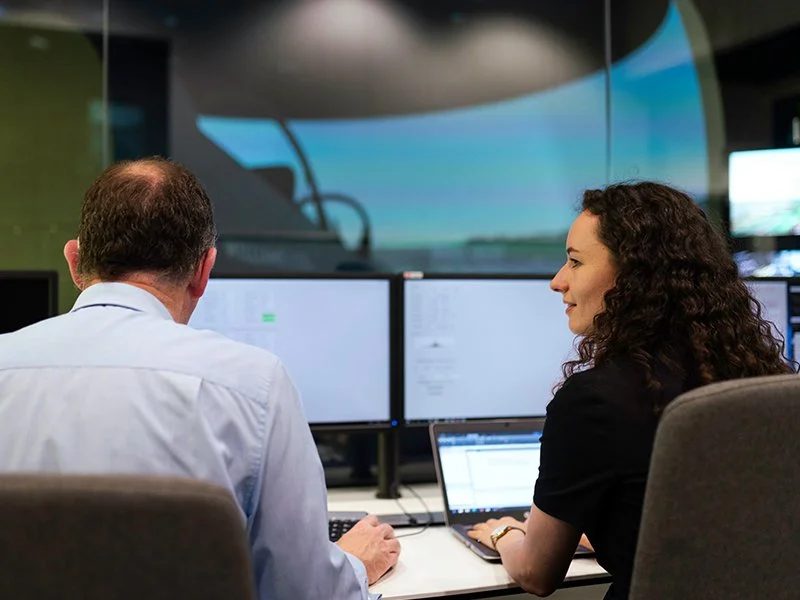 Man and woman working on laptops in front of larger computer screens — Cherokee Federal Cloud Engineering & Migration