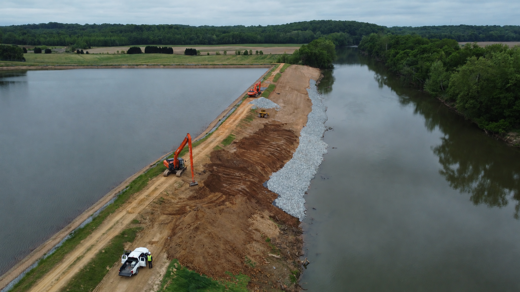 Aerial view of construction equipment and a white pickup on an embankment between water basins