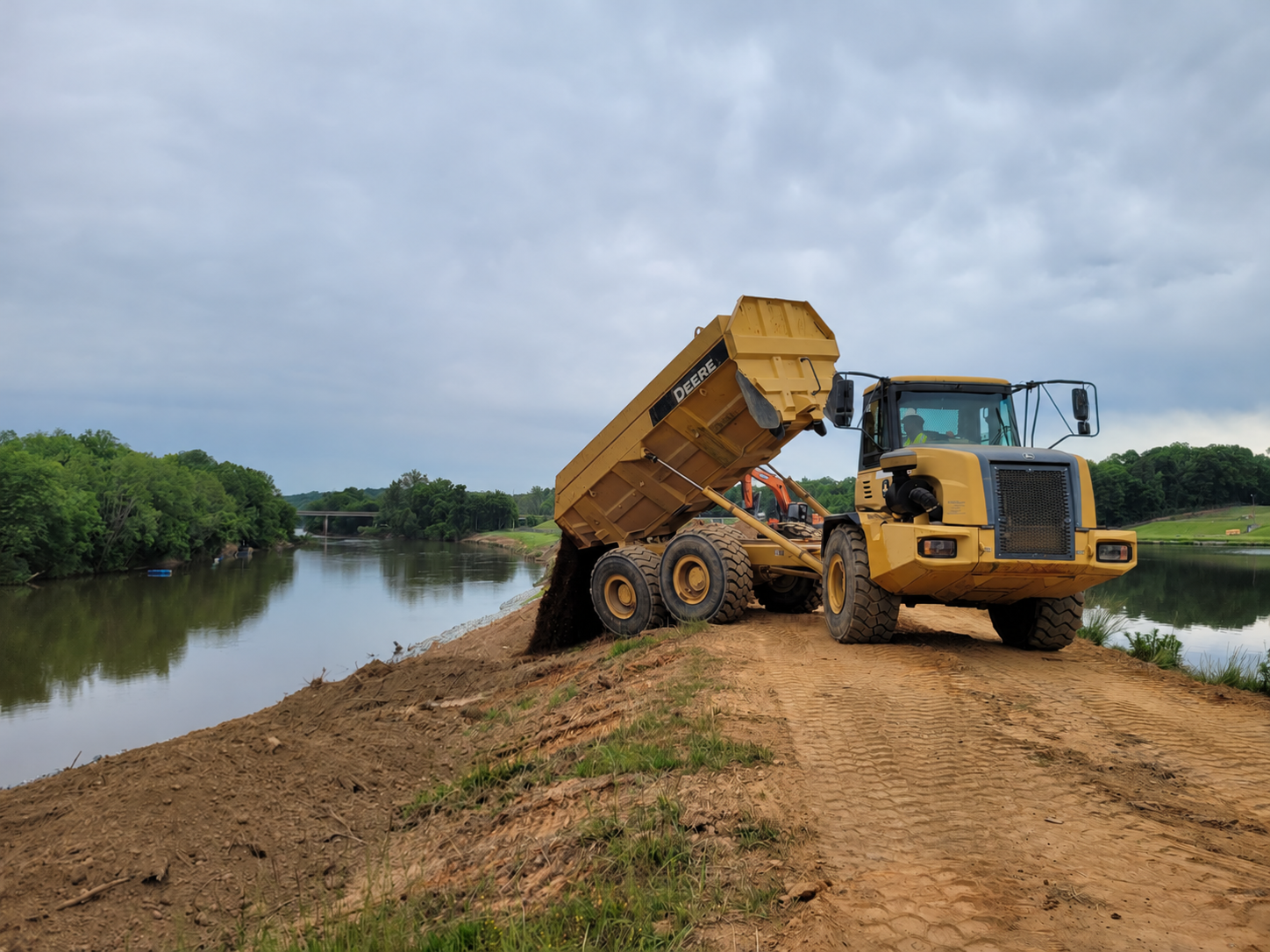 Yellow articulated dump truck with its bed raised beside water