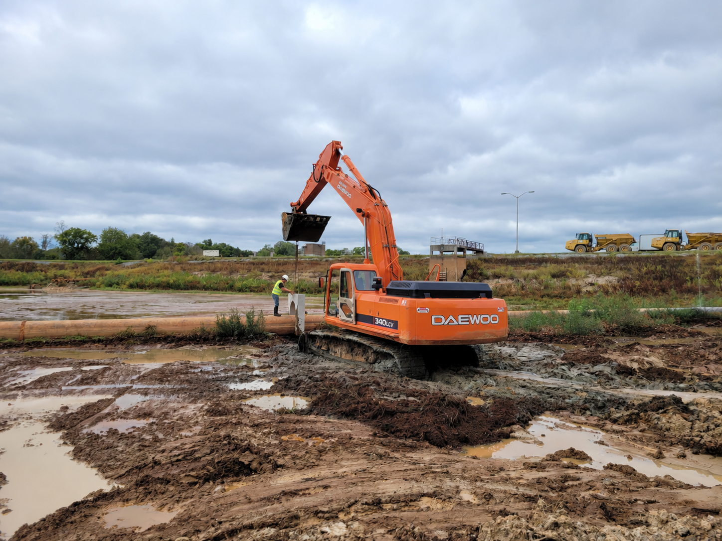 Orange excavator, pipe, and a worker on a muddy construction site