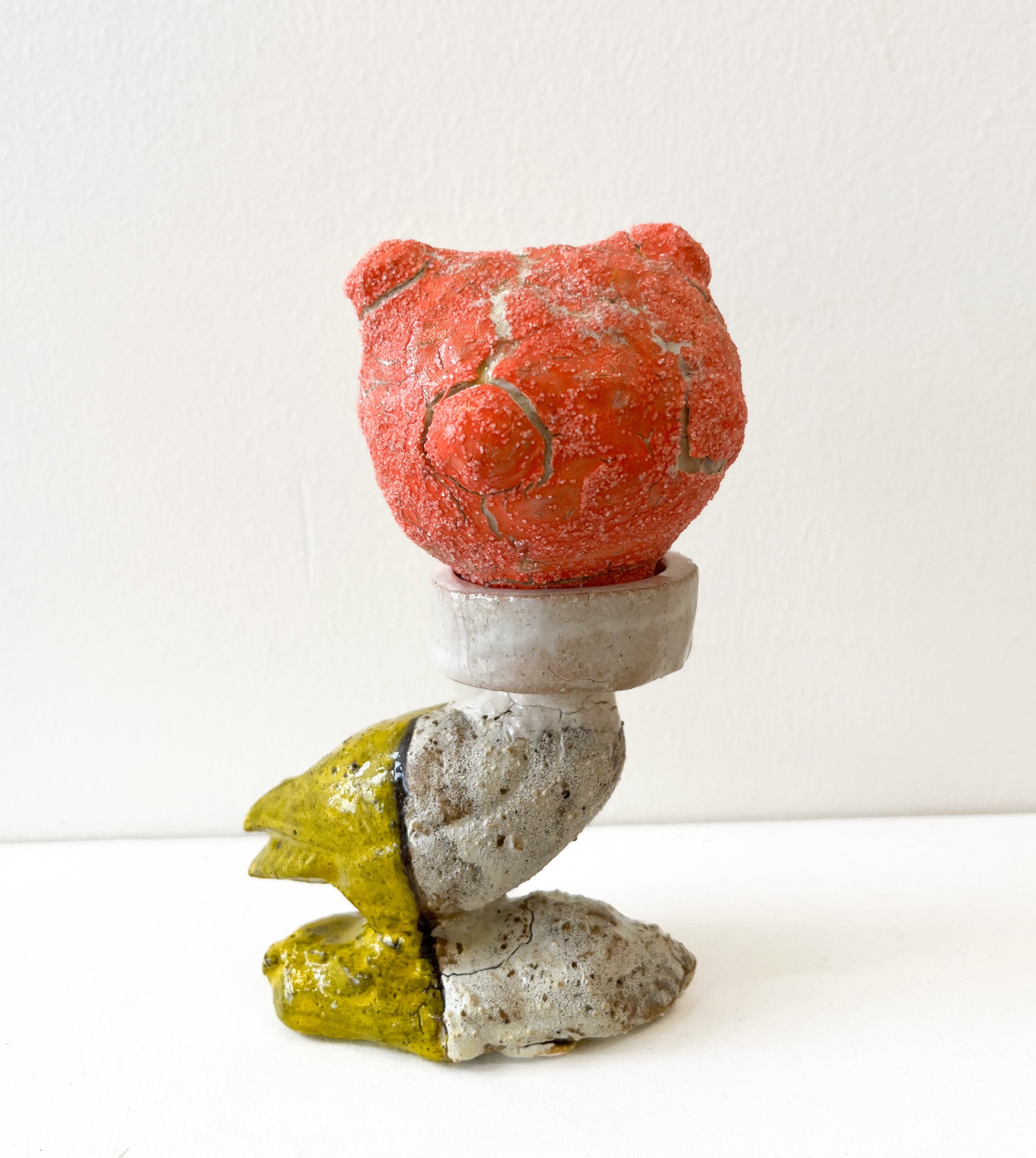 Textured sculpture with a red head and yellow and pale fragments.