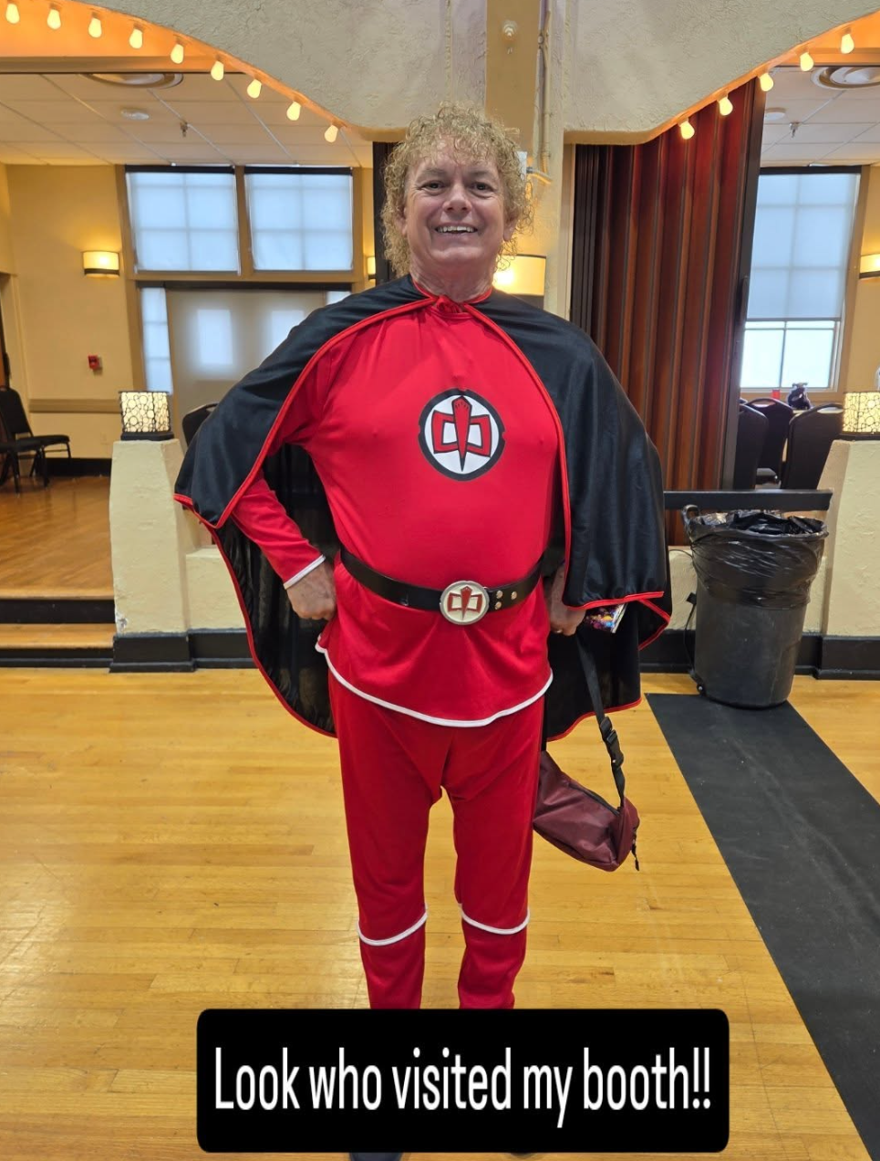 Convention visitor in a red costume and black cape, photographed near the booth