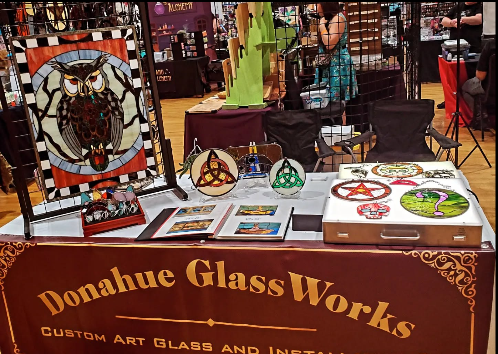 Donahue Glassworks convention booth with owl panel, colorful stained glass and burgundy studio banner