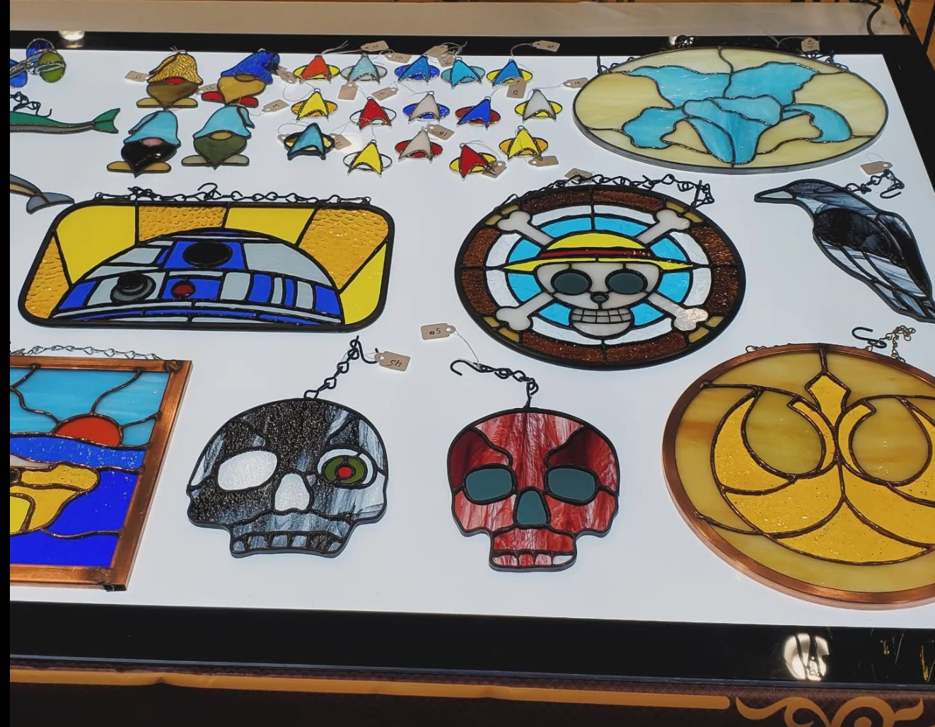 Stained glass arranged on an illuminated display including a droid, skulls, small badges and flower panel