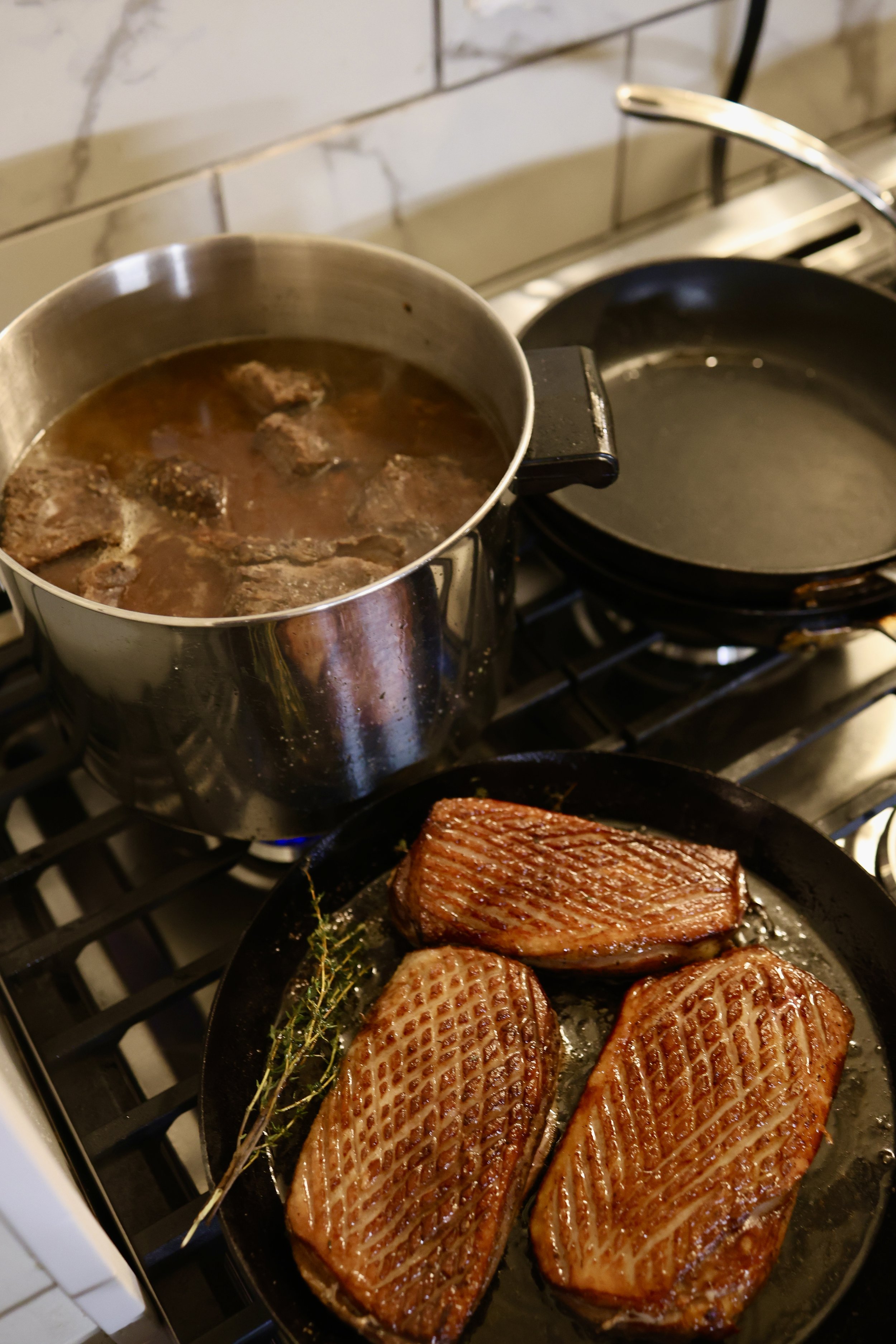 Duck breast and short ribs cooking on a stovetop at a private dinner