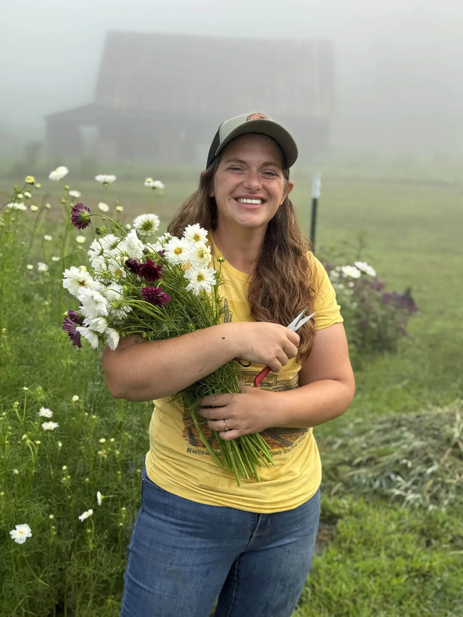 Flower grower holding freshly harvested blooms in a misty farm field