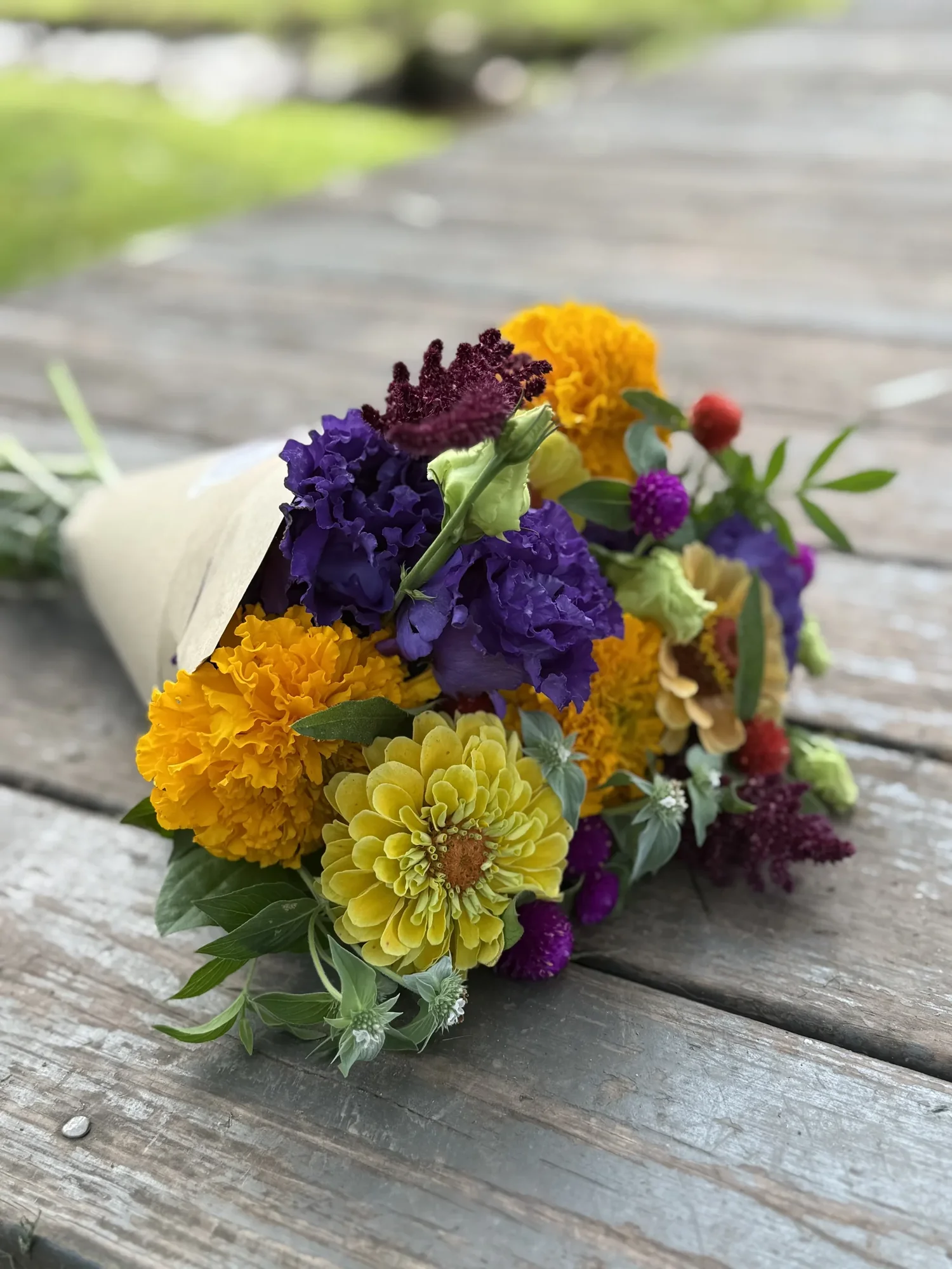 A wrapped seasonal farm bouquet resting on a wooden table