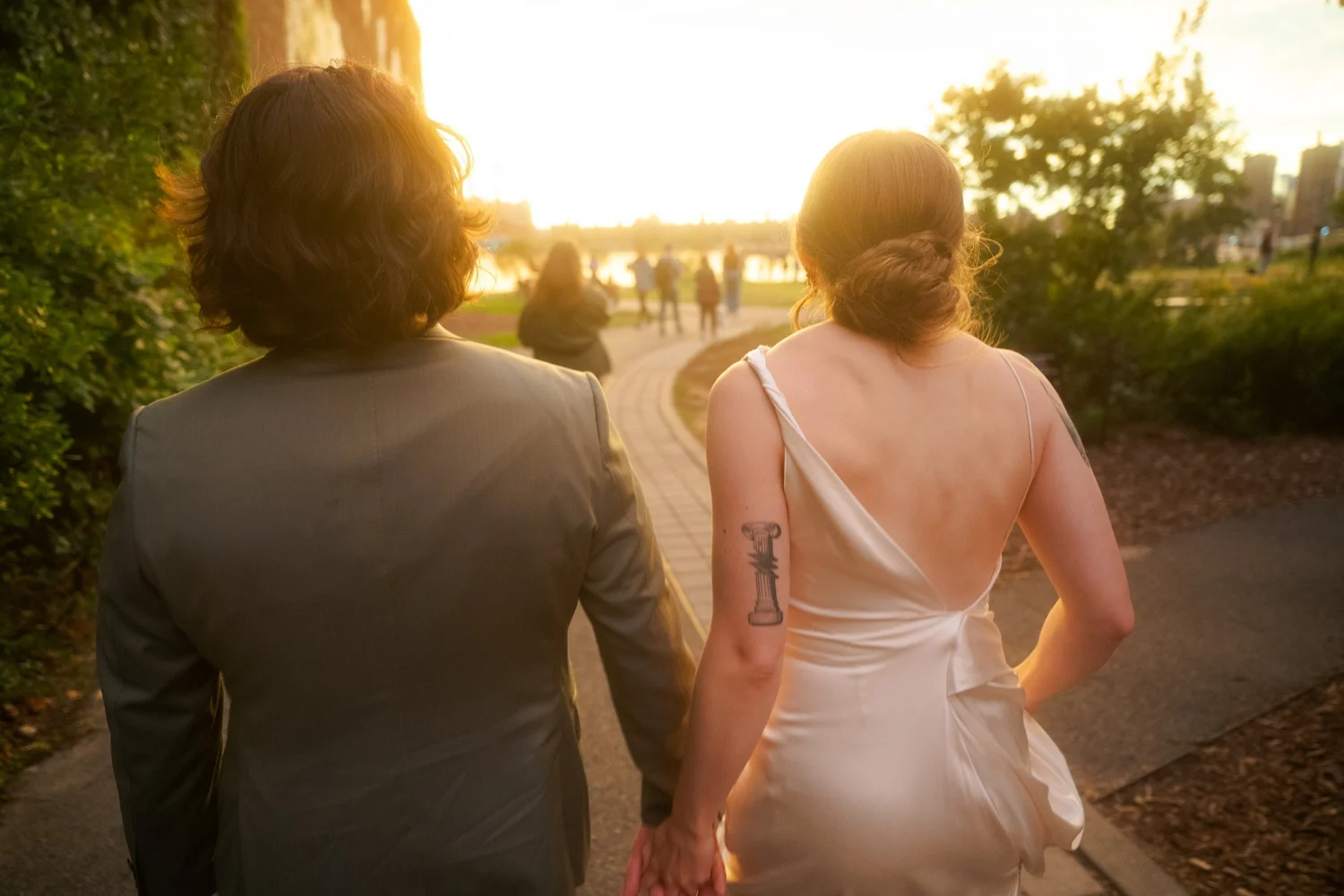Bride and groom walk hand in hand into golden light in the waterfront park next to Neptune Room, Greenpoint
