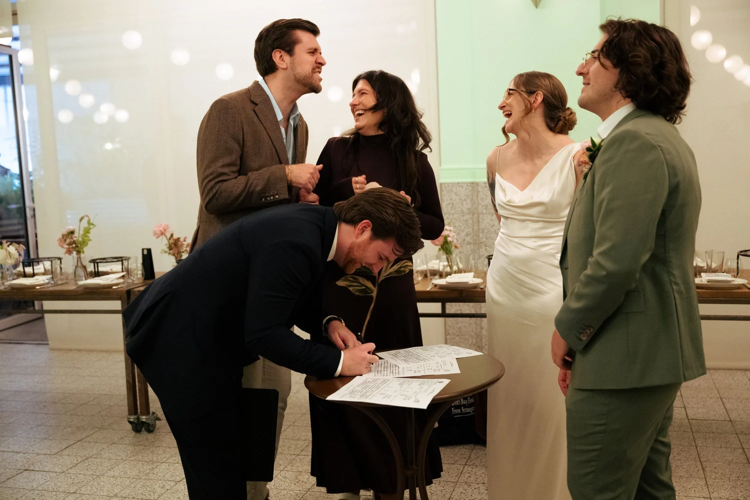 Couple laughs as a friend signs the marriage license