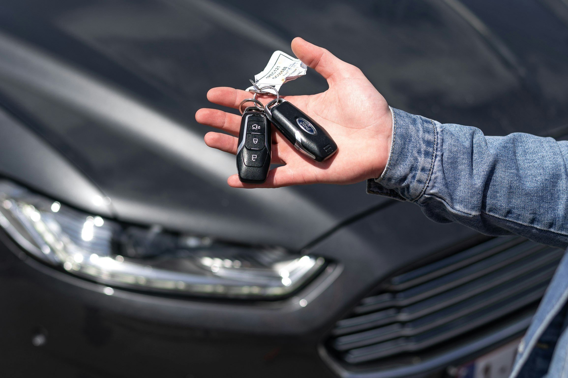 Car keys held beside a vehicle