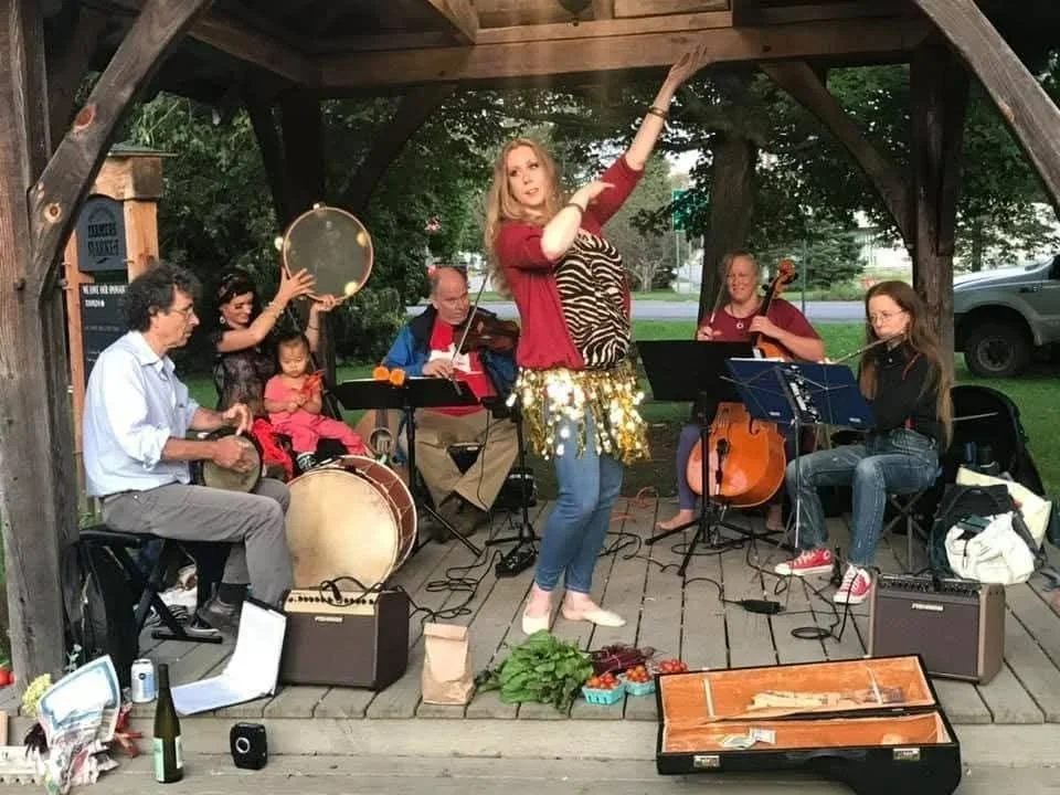 Original outdoor performance photo with musicians and a dancer beneath a wooden pavilion