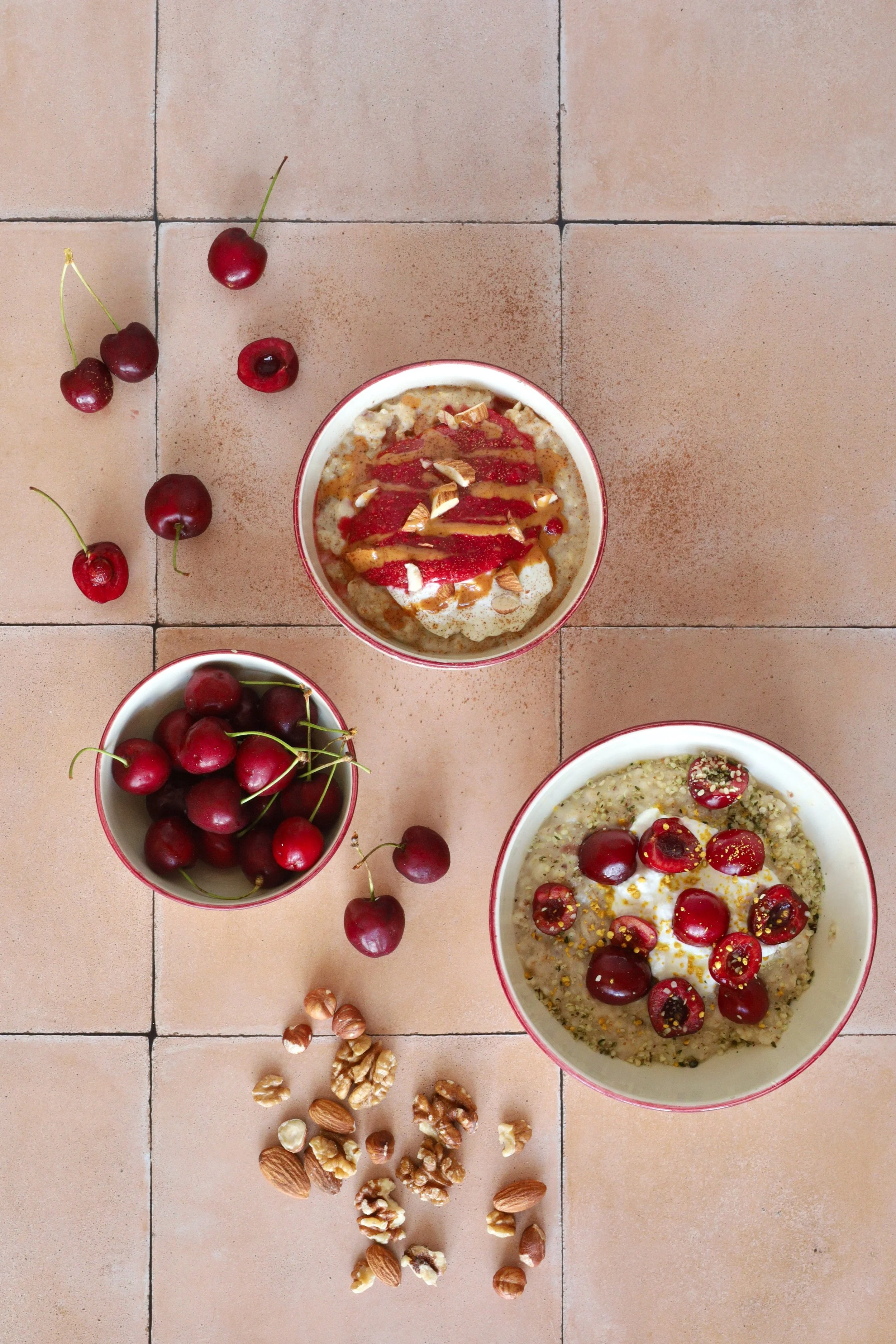 Two bowls of everyday oats with bowl of cherries and cherries on table nearby