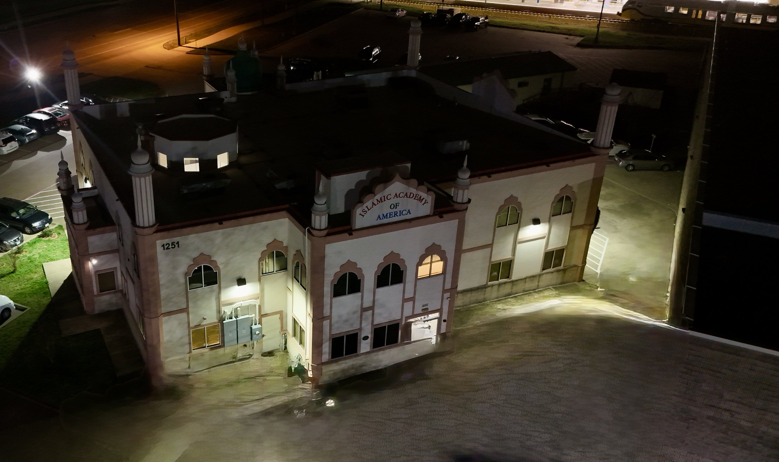 Aerial view of an illuminated building and its surrounding grounds after dark.