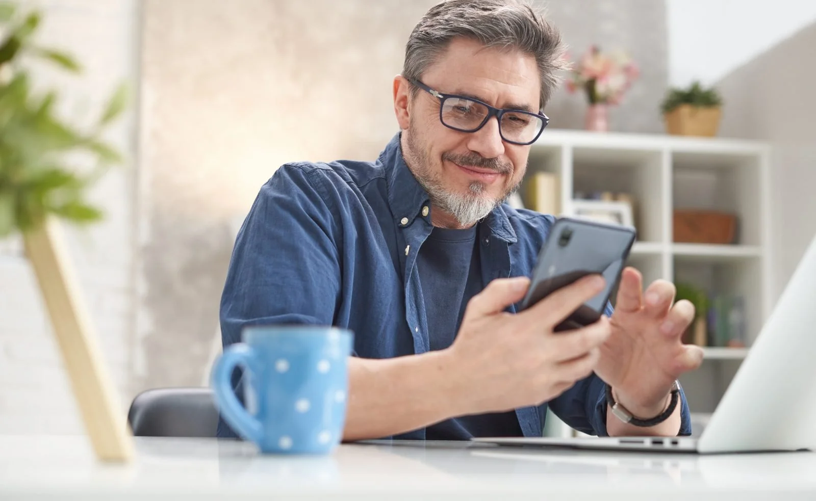 A man at his kitchen table smiling at a message on his phone