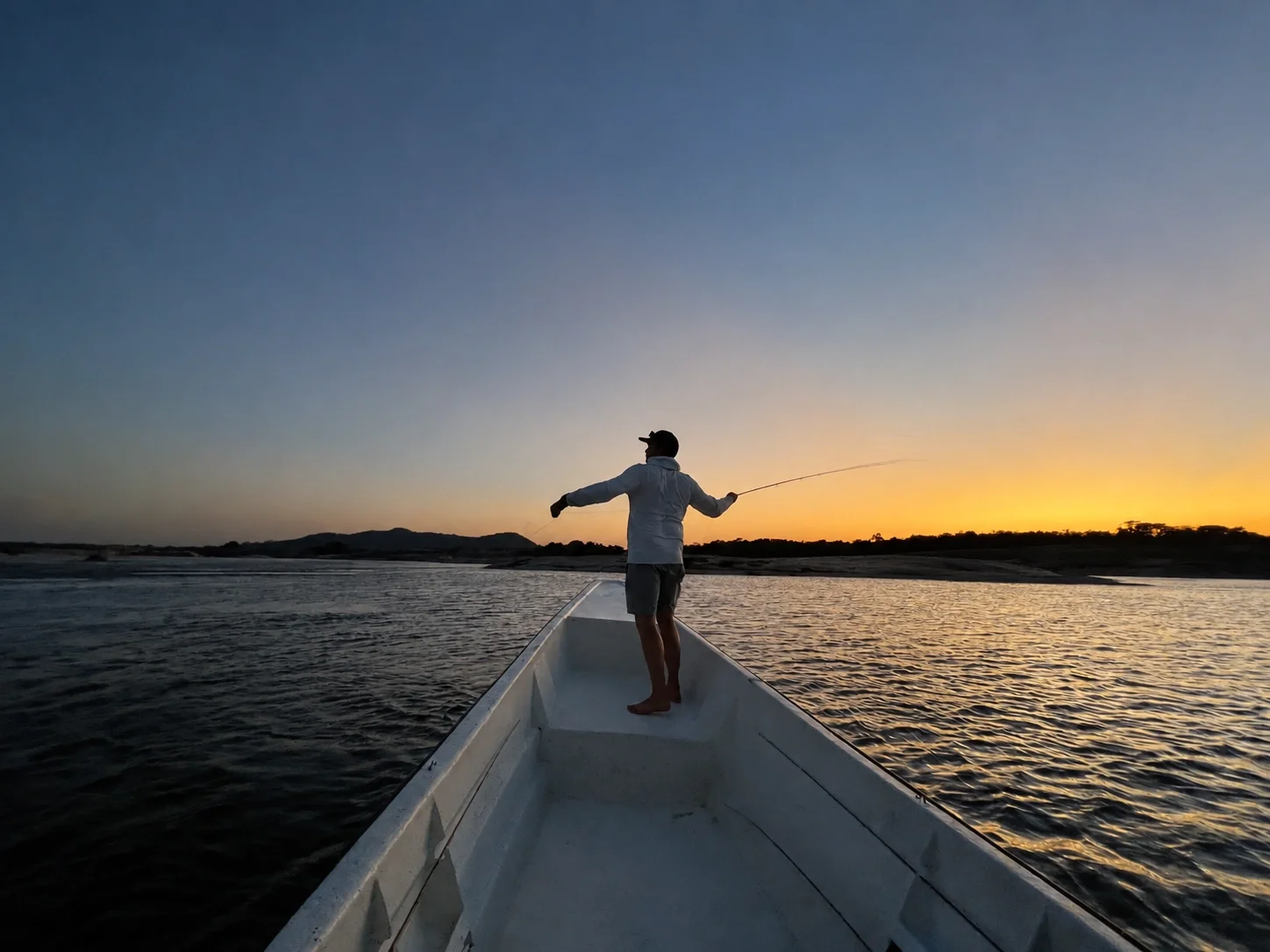 Angler standing in a boat on a river at sunset