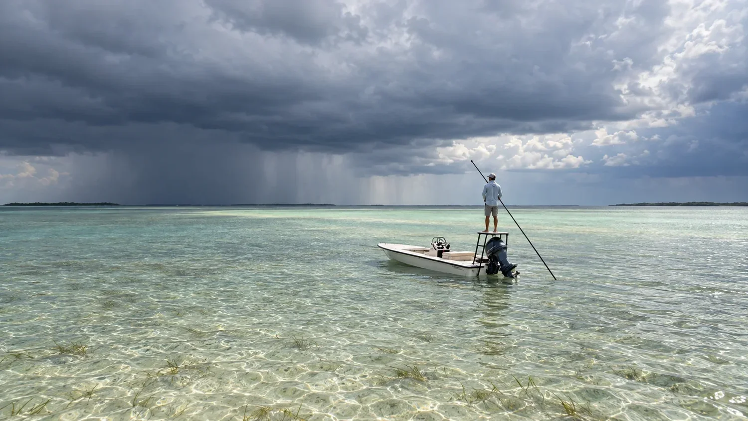 A skiff on a shallow, clear flat under a dark band of cloud and rain, with the sky clearing on the right.