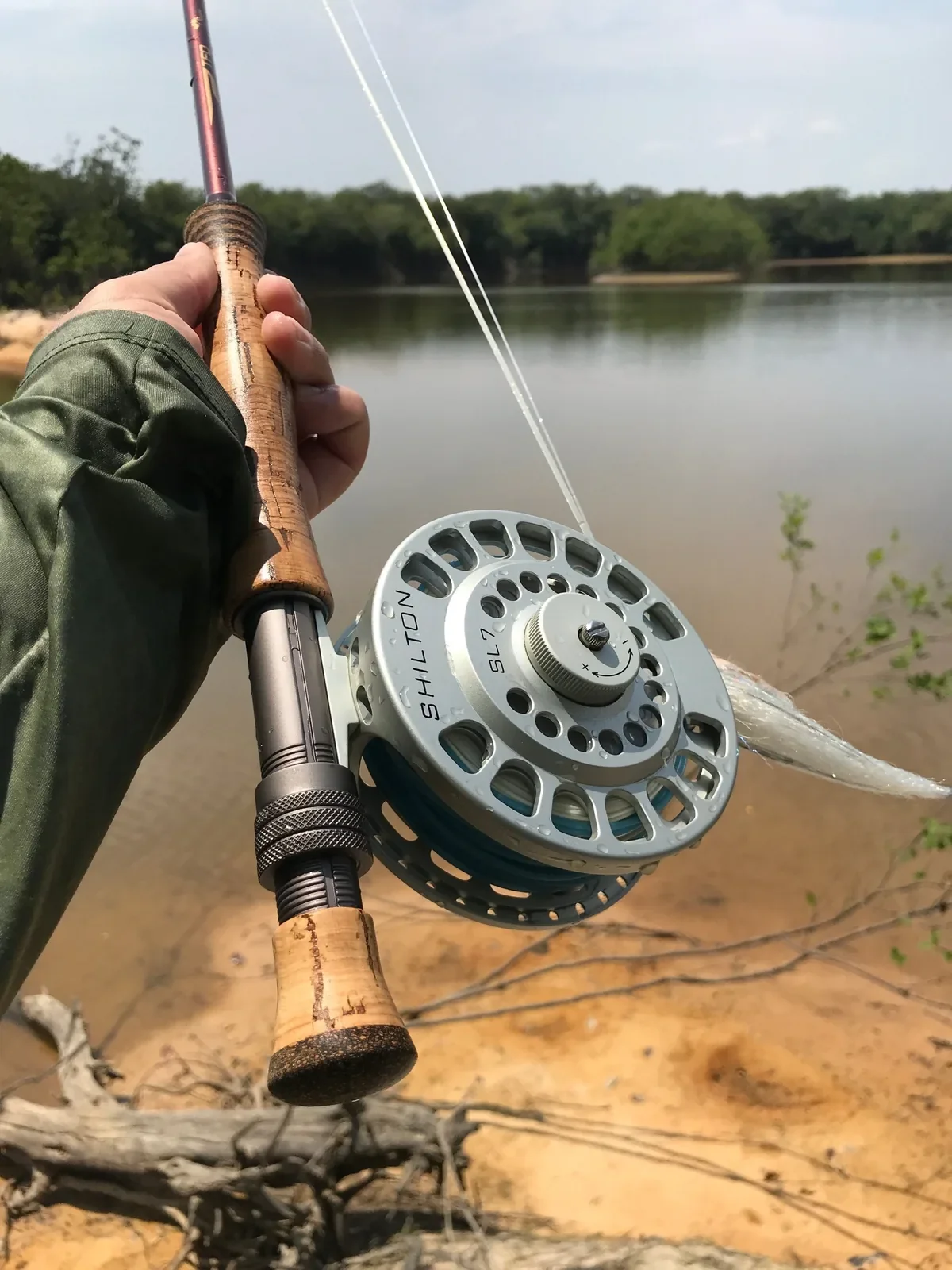 Hand holding a fly rod and large reel loaded with bright tropical fly line over a sandy lagoon shore