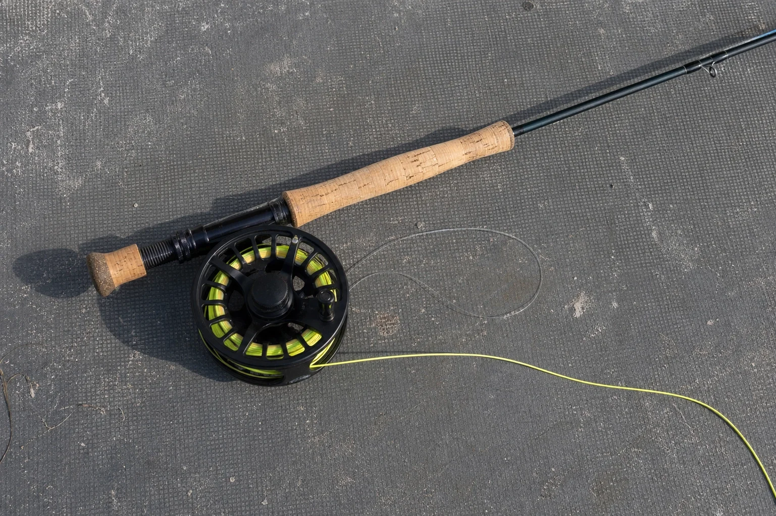 Flat-lay of an 8-weight fly fishing setup on a gray skiff deck &mdash; cork grip rod, large-arbor saltwater reel, chartreuse tropical floating line coiled alongside.