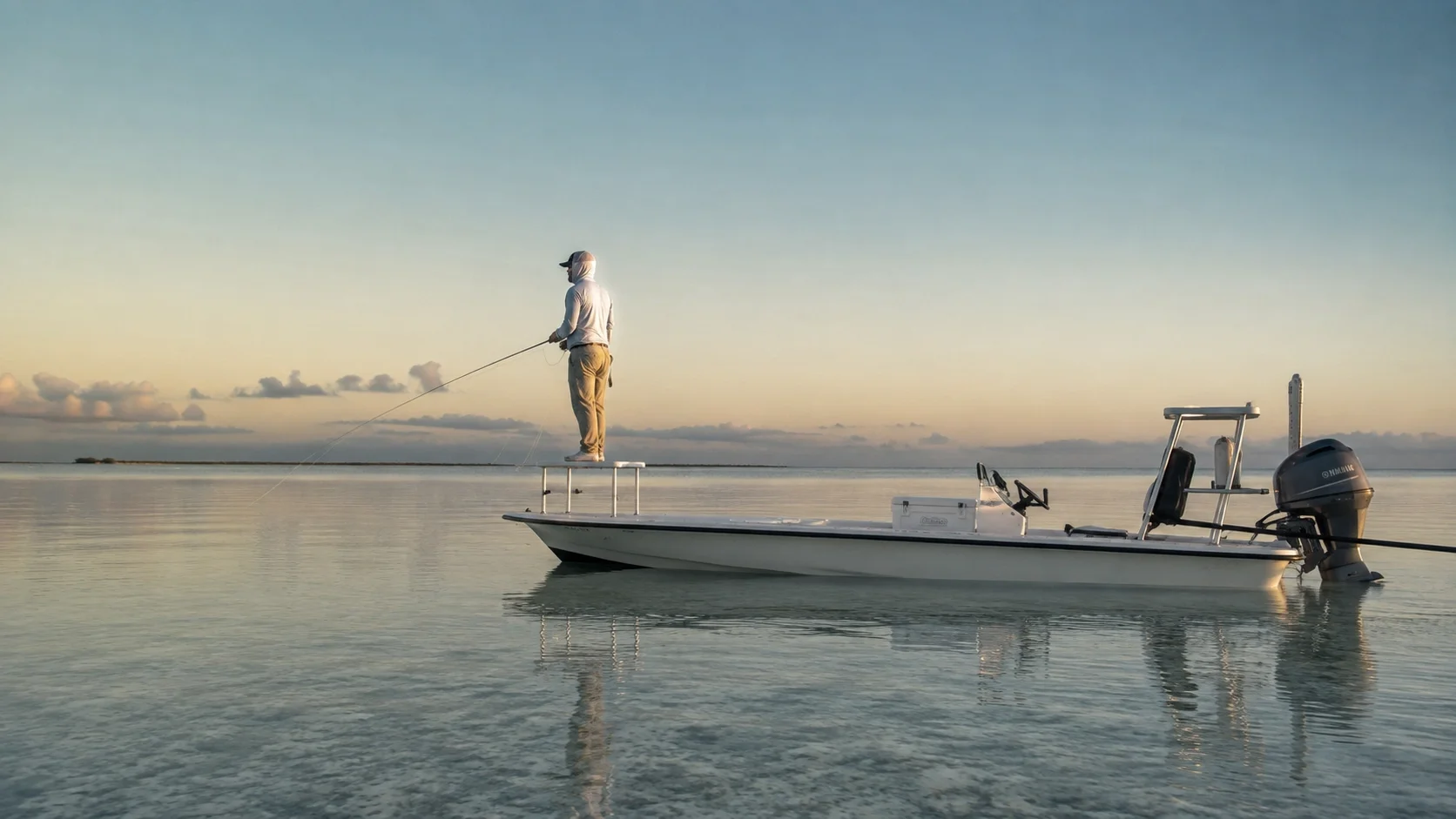 Fly angler scanning for tarpon from a skiff bow at first light on the flats