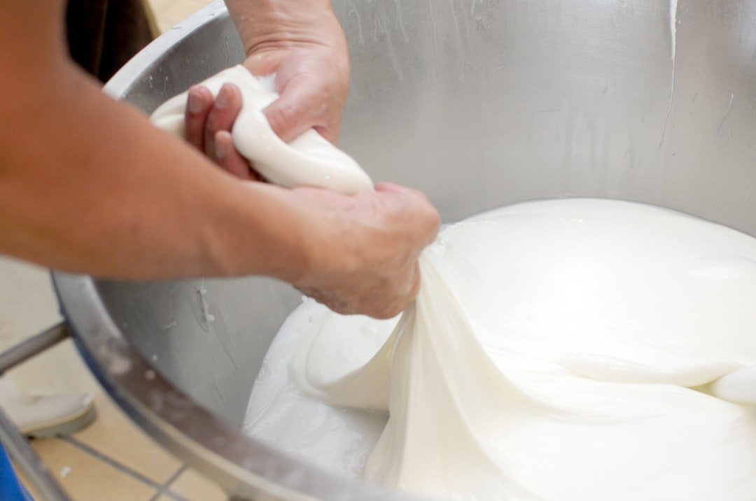 A cheesemaker stretches fresh white cheese by hand over a metal vat.