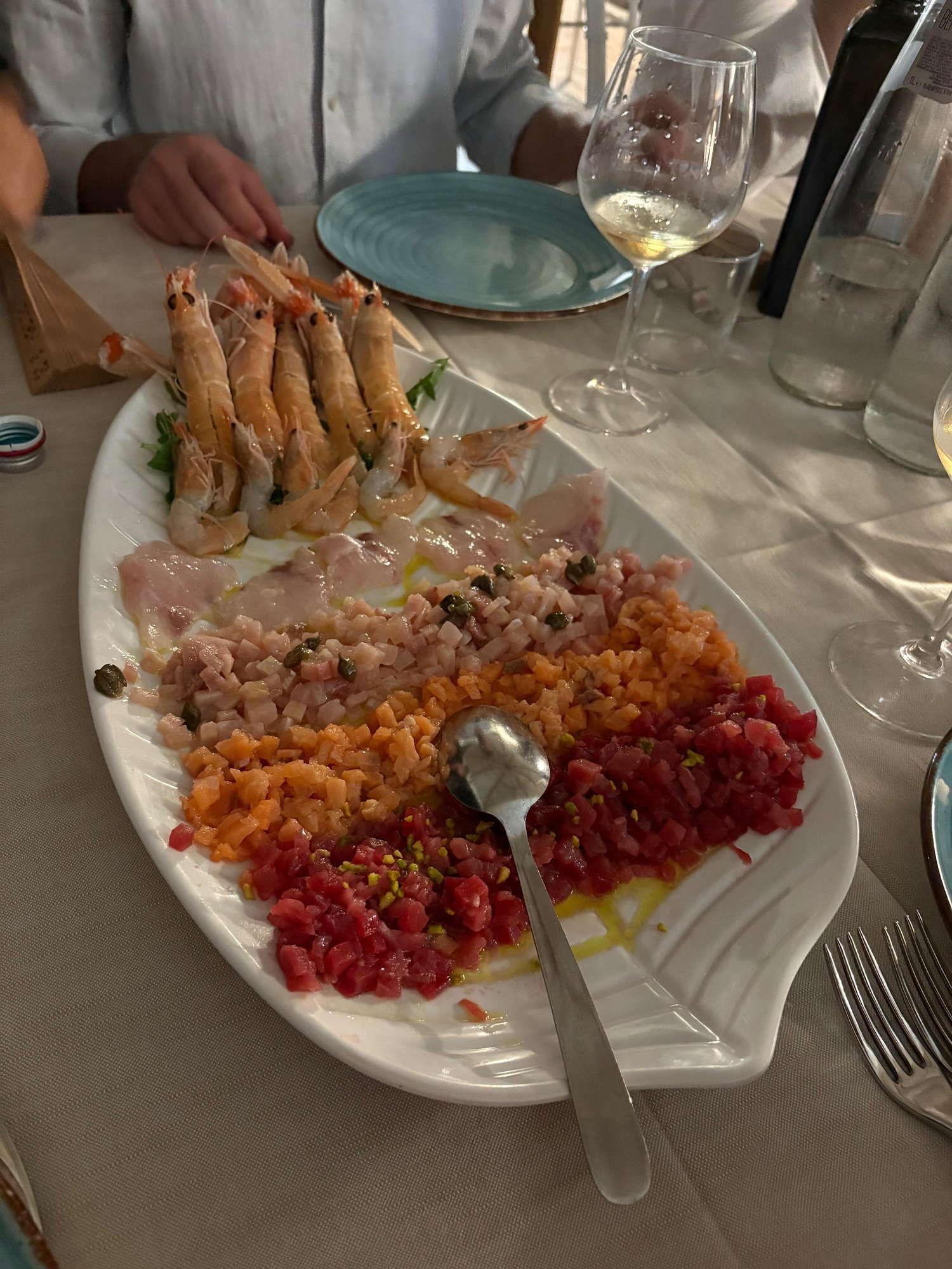 A platter of seafood at a shared table, with hands, plates and wine glasses around it.