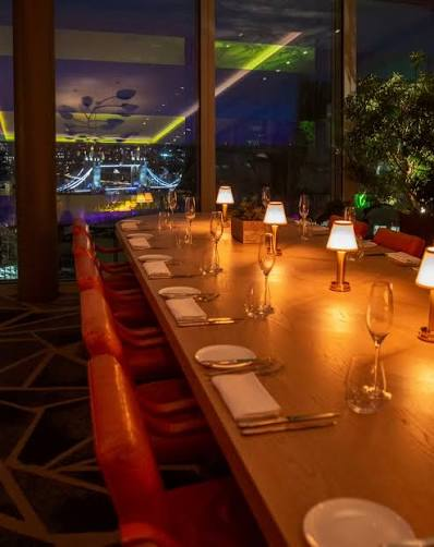 The long dining table at 14 Stories with London lit up at night beyond the windows