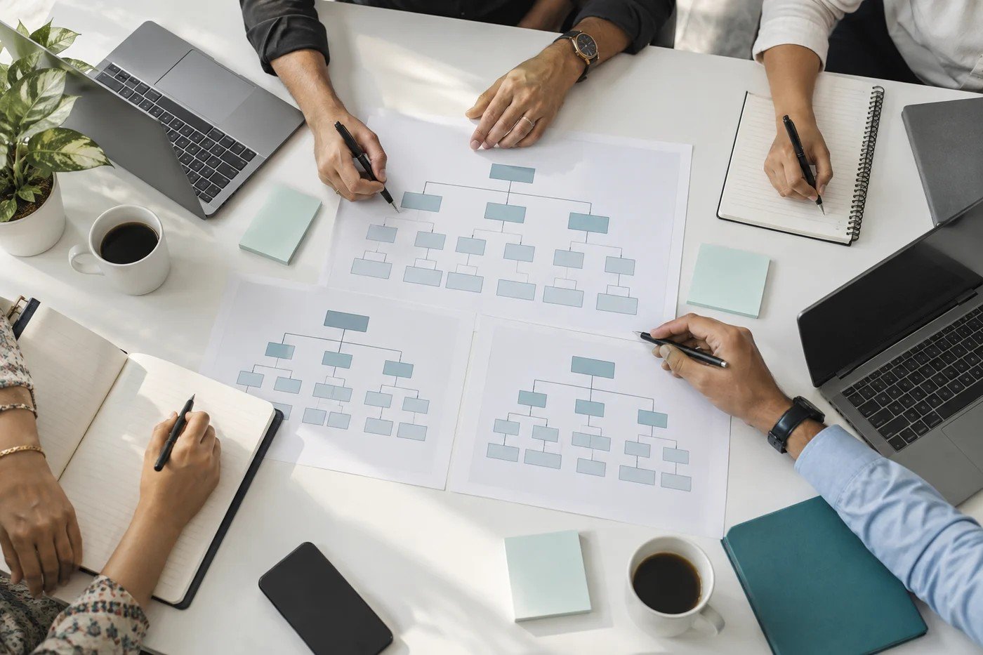 Illustrative overhead photograph of a planning table with charts, notes, laptops and participants’ hands