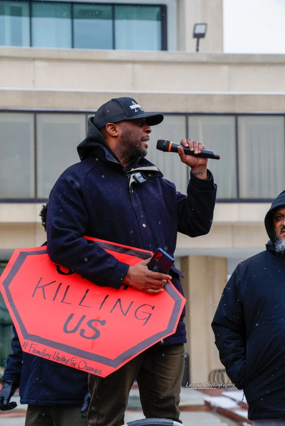 Thomas Kearney speaks into a microphone at an outdoor demonstration. Photograph by Lazore Photography.