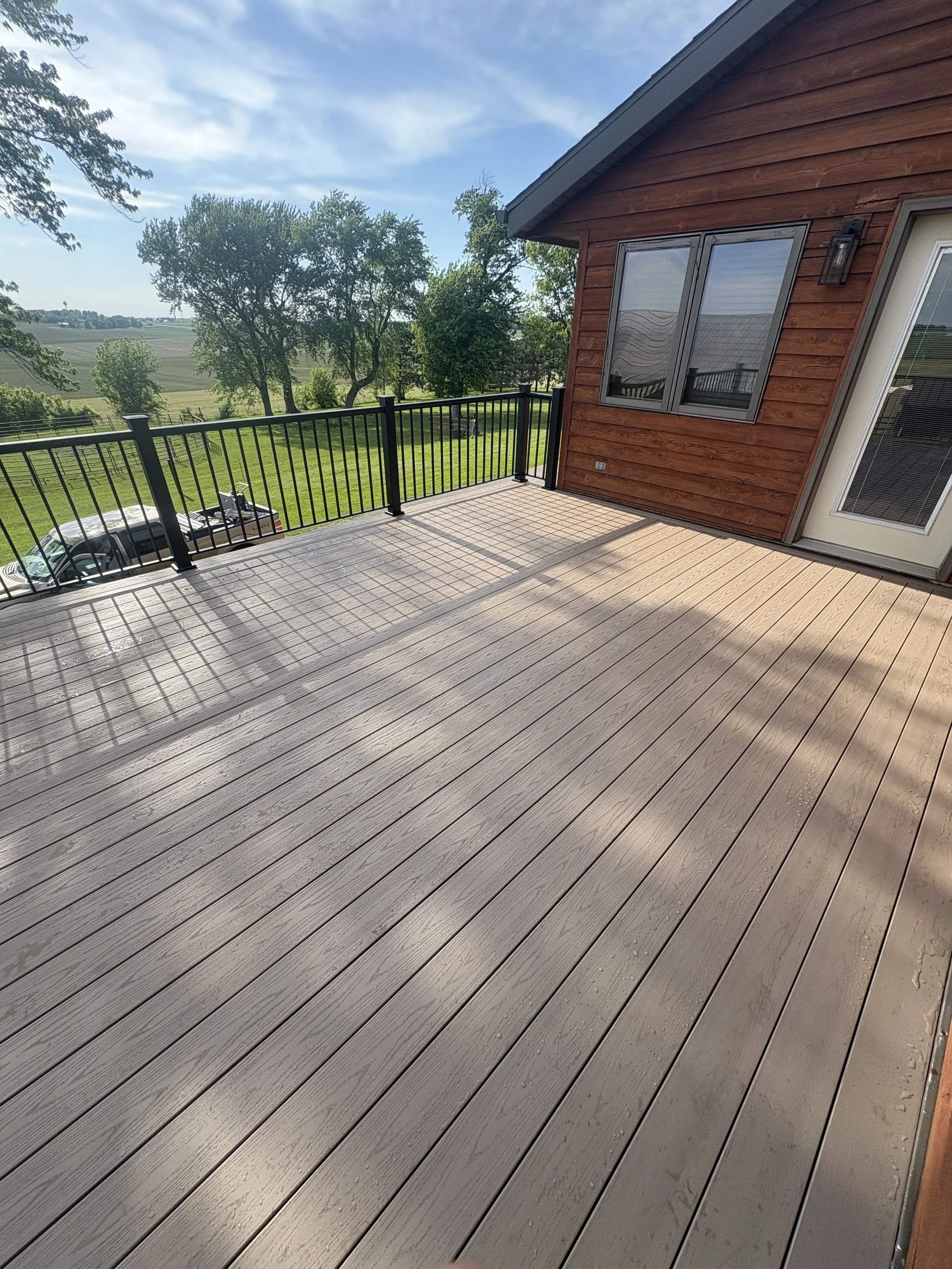 Completed composite deck with black railing beside a wood-sided home
