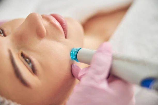 Close-up of a woman receiving a hydrodermabrasion facial treatment with a blue-tipped wand to exfoliate and hydrate the skin.