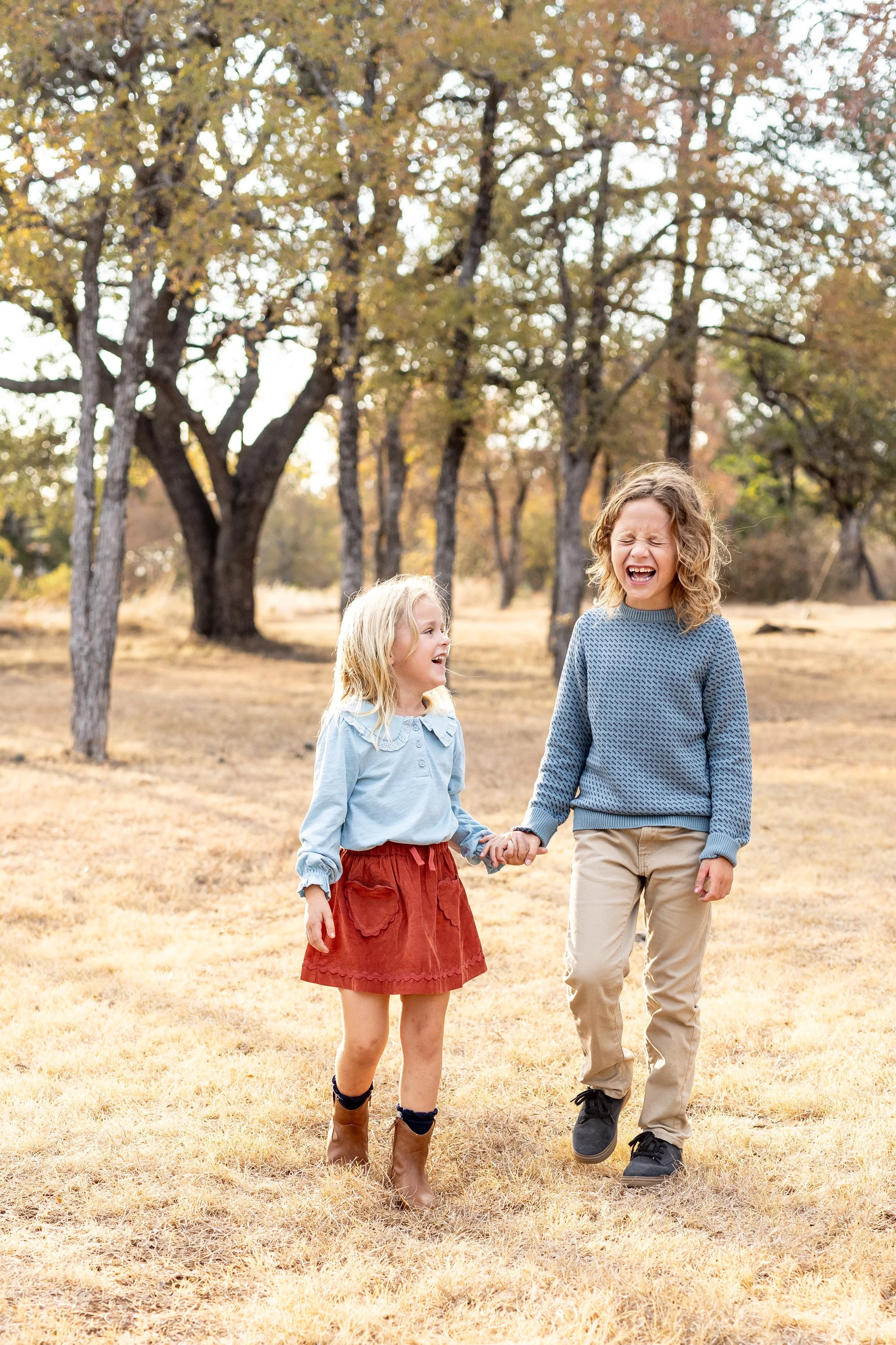 Two kids in pale blue and rust holding hands in a field