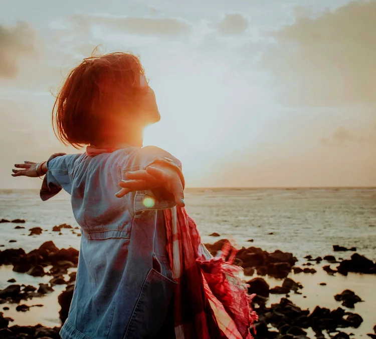 Woman with open arms facing the sunset by the sea, representing past life regression in Orlando