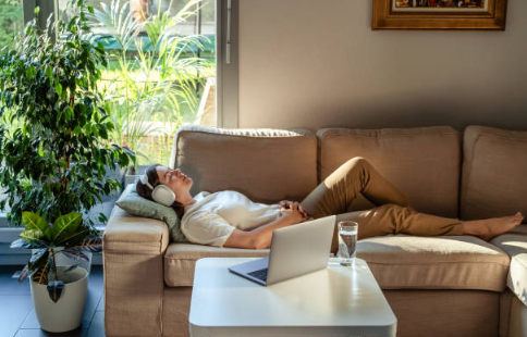 Woman relaxing on a sofa with headphones during an online trauma-informed hypnotherapy session