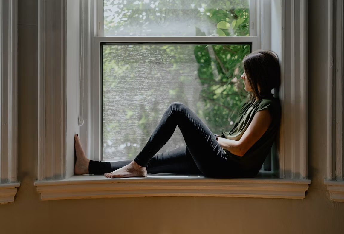 Woman sitting on a windowsill looking outside in soft natural light, quietly reflecting