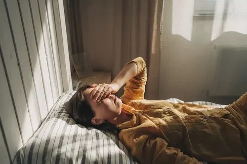 Woman lying in bed with her hand over her face, representing grief and loss
