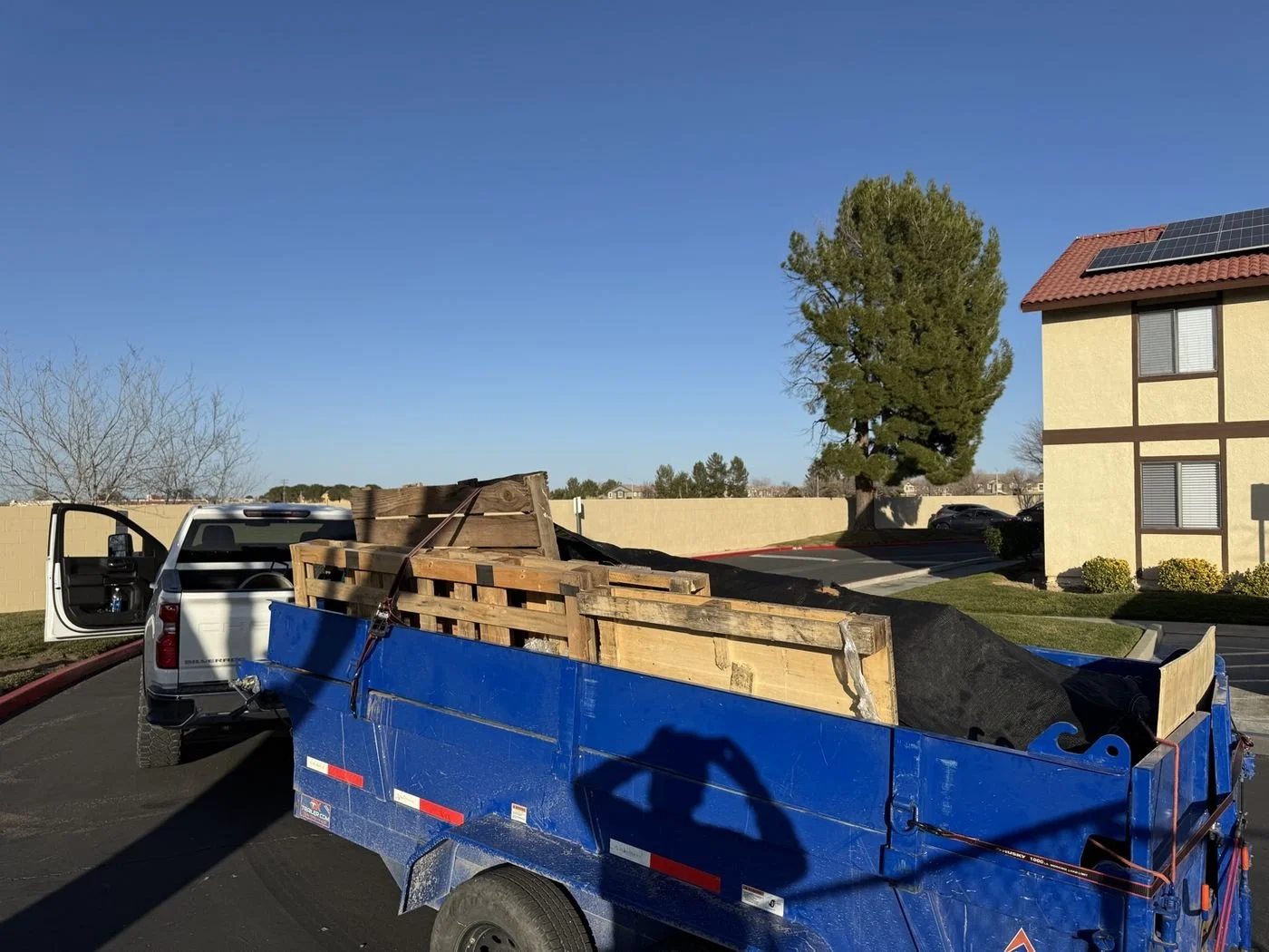 Blue RawMaxx dump trailer loaded with wood pallets and tarped debris at an apartment complex