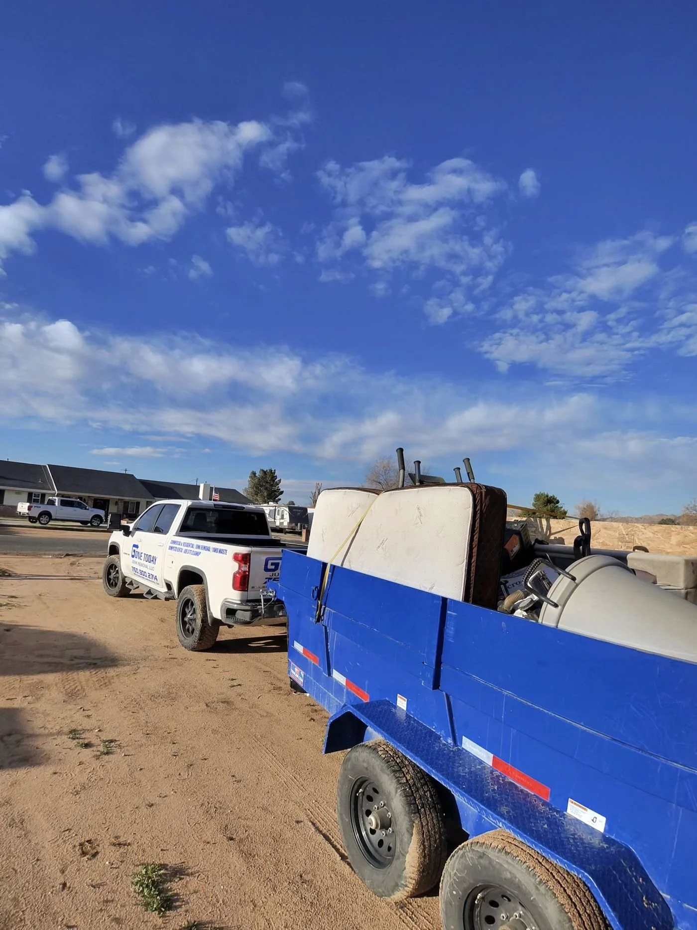 White Gone Today Junk Removal branded pickup truck towing the blue dump trailer loaded with mattresses and junk