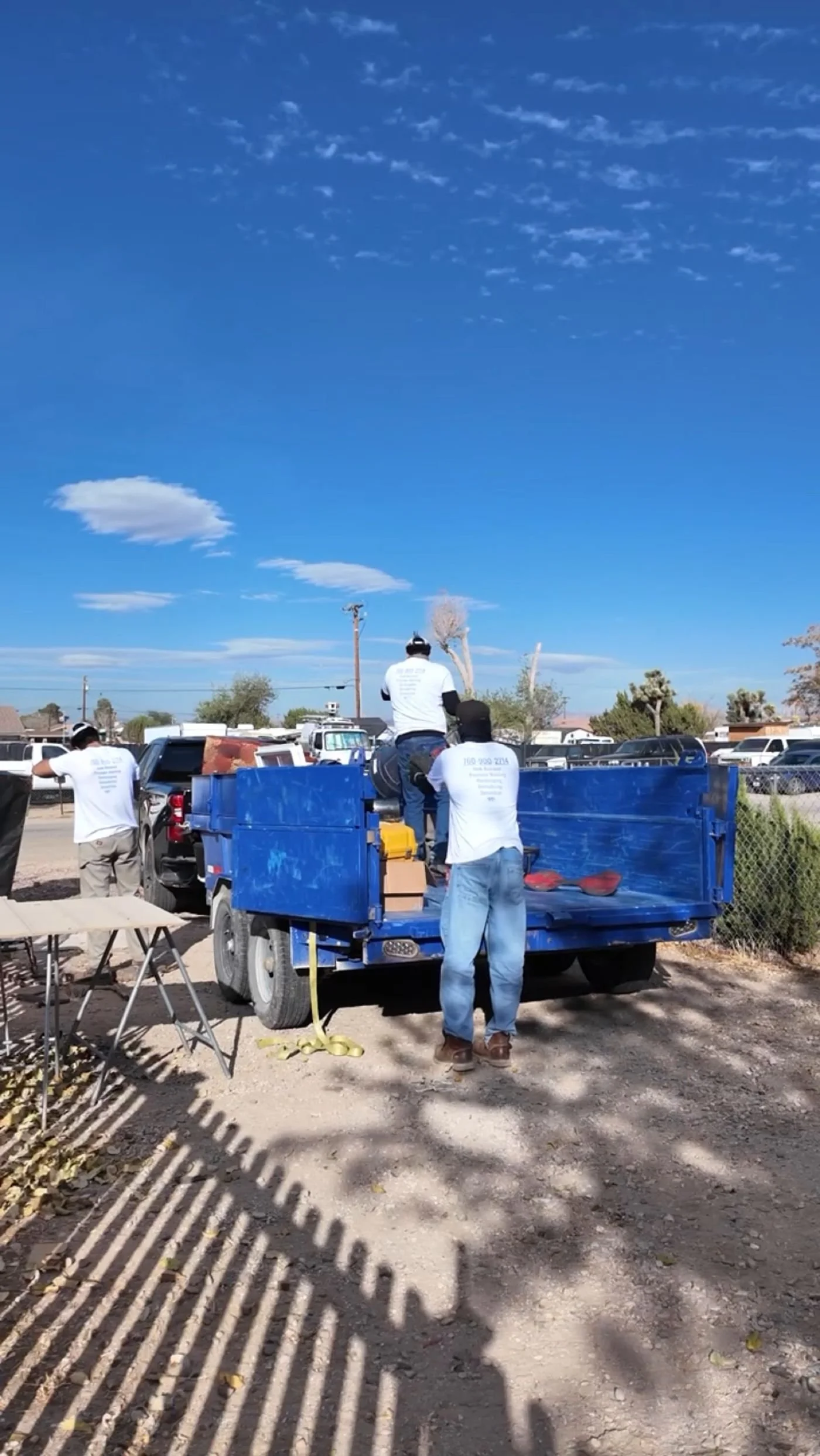 Gone Today crew in white shirts loading junk into the blue dump trailer on a sunny High Desert day