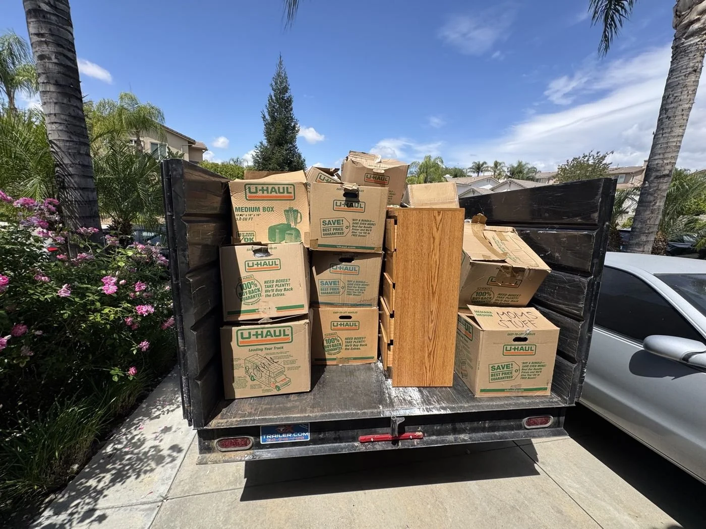 Black dump trailer stacked with moving boxes and a wood dresser in a residential driveway